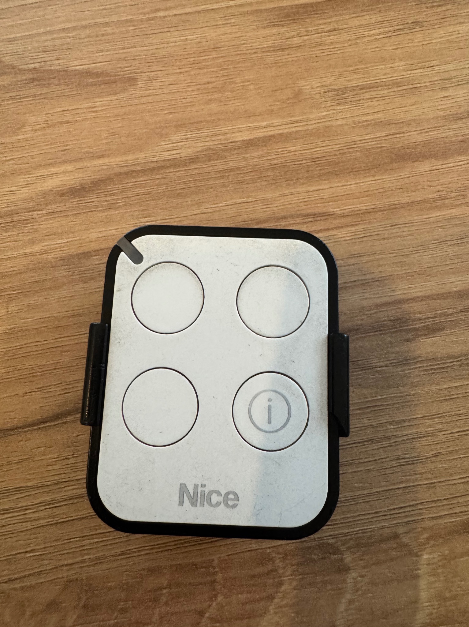 Pilot do bramy firmy Nice z czterema okrągłymi przyciskami leżący na drewnianym blacie.