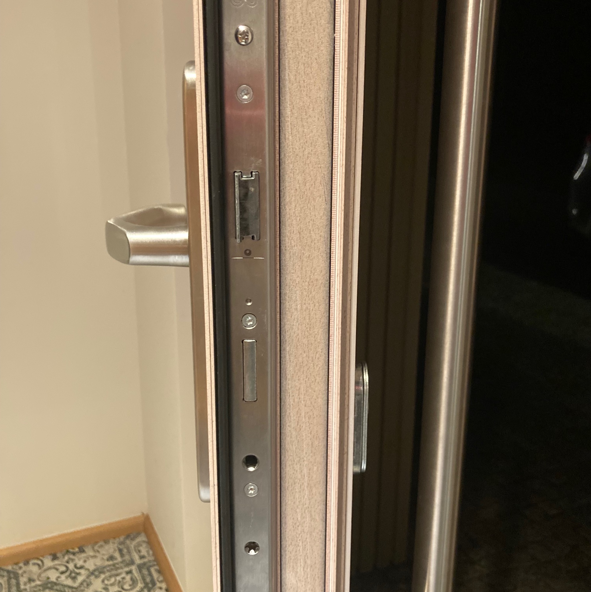 Widok na zamek i uszczelkę w otwartych drzwiach wejściowych, widoczna metalowa klamka i fragment futryny.