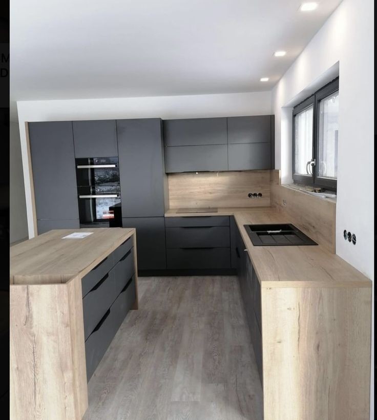 Nowoczesna kuchnia: ciemnoszare szafki z drewnianymi blatami, wyspa kuchenna z szufladami, oświetlenie punktowe i okno z czarną ramą.