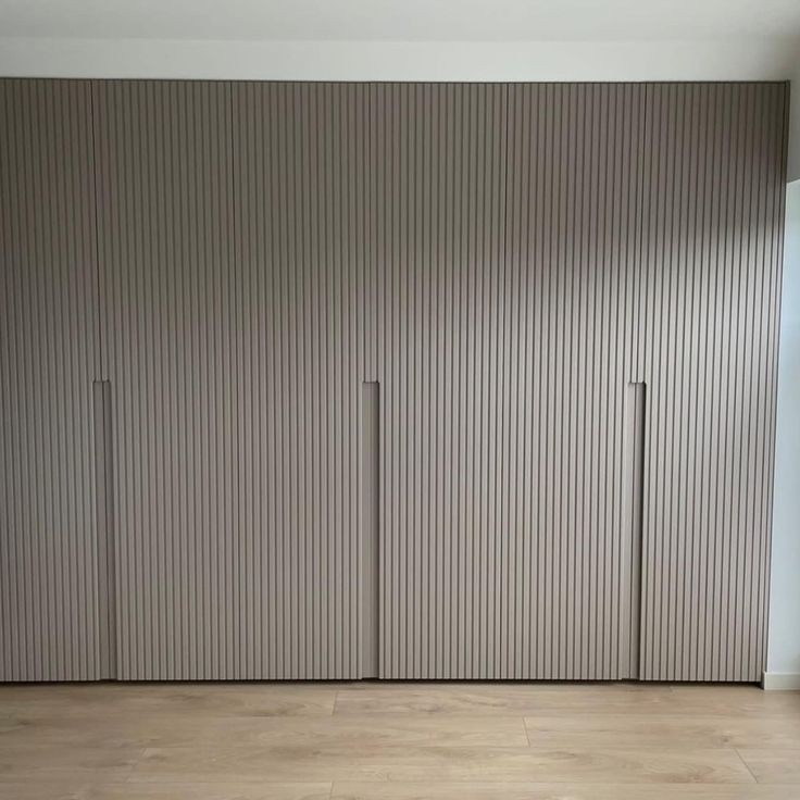 Szafa wnękowa z ryflowanymi frontami w odcieniach beżu, zintegrowane uchwyty, na podłodze panele drewniane.