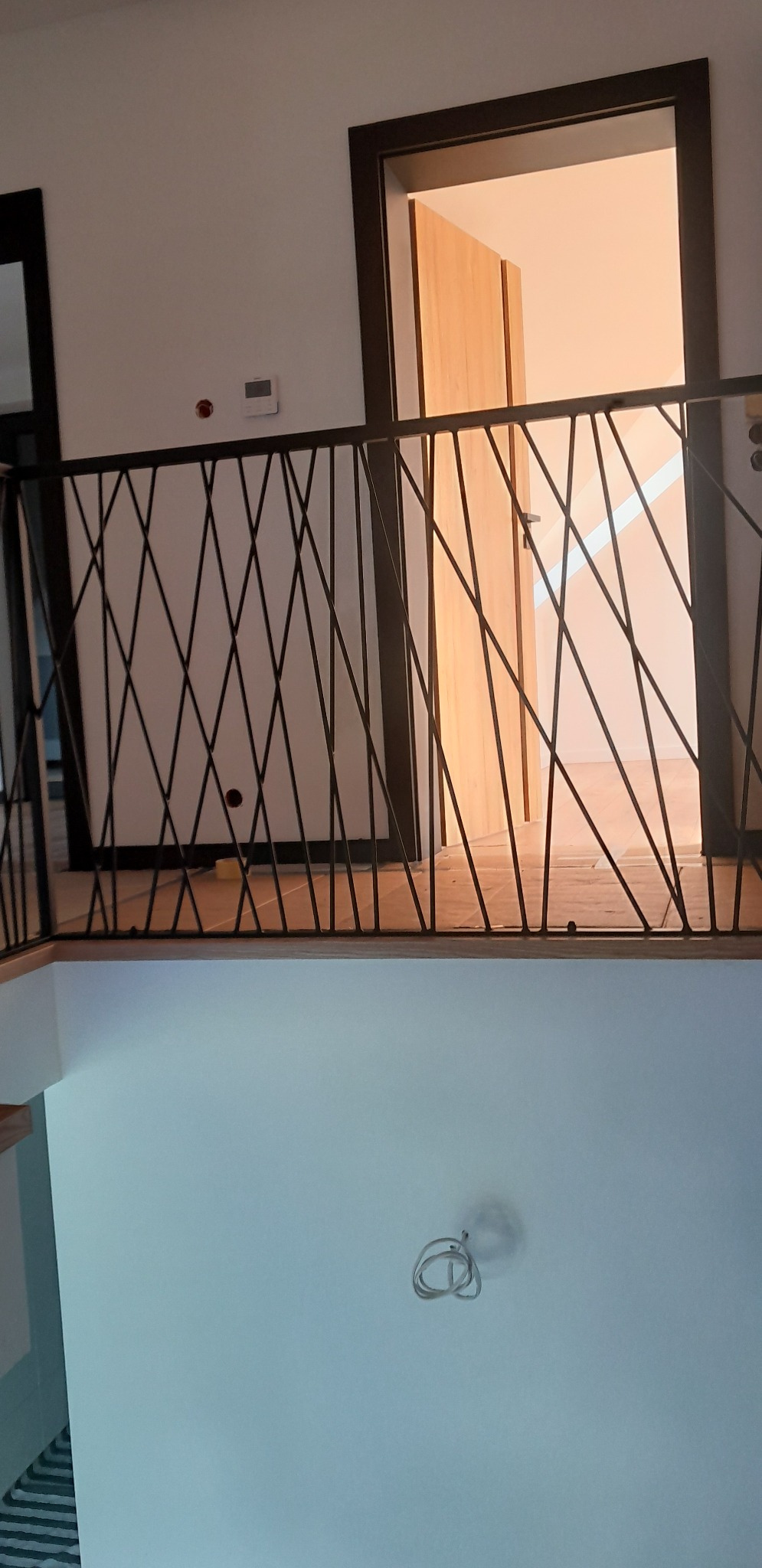 Nowoczesna balustrada schodowa z czarnych, krzyżujących się prętów na tle jasnych ścian i otwartych drzwi do pokoju.