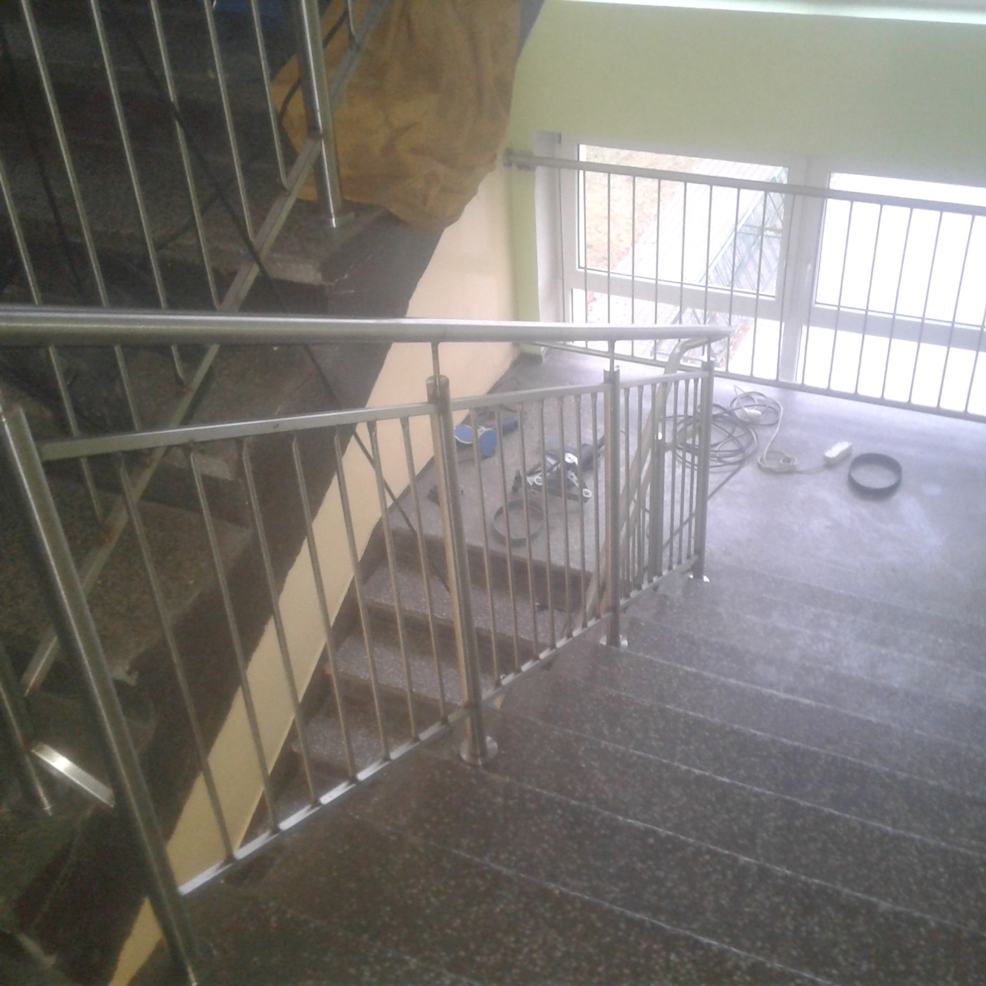 Metalowa balustrada schodowa z widocznymi śladami prac montażowych, w tle narzędzia i kable na schodach.