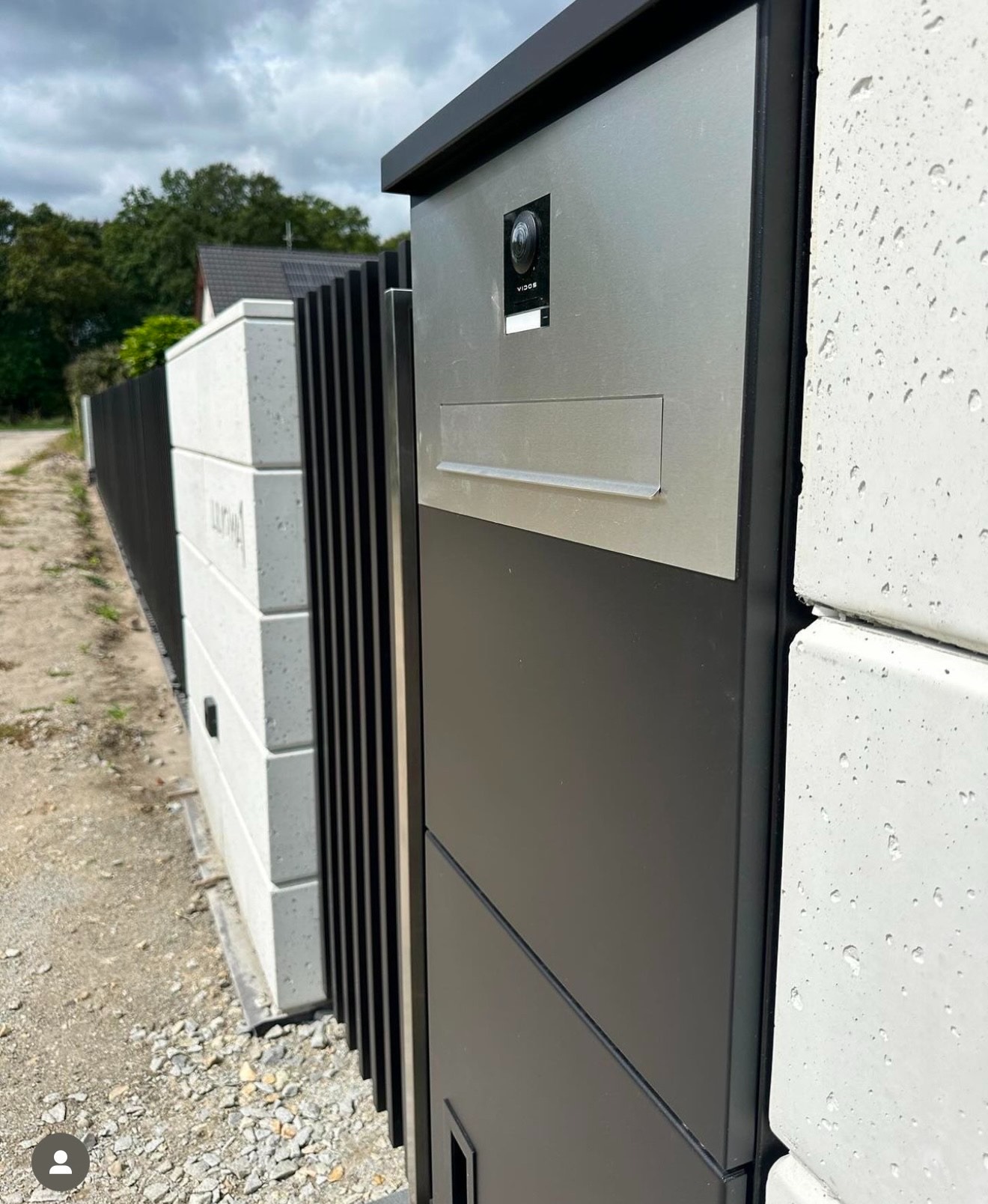 Nowoczesne ogrodzenie z elementami betonowymi i metalowymi, zintegrowana skrzynka na listy i wideodomofon, widok z bliska na fragment ogrodzenia.