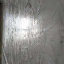 WTL-BUD - Ściana pokryta szarą, dekoracyjną strukturą z widocznymi smugami i odbiciem światła, ukazana pod kątem.