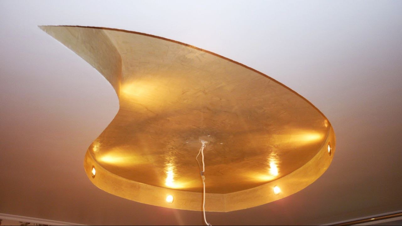 Dekoracyjna, złota struktura na suficie z oświetleniem punktowym, przypominająca abstrakcyjną rzeźbę.