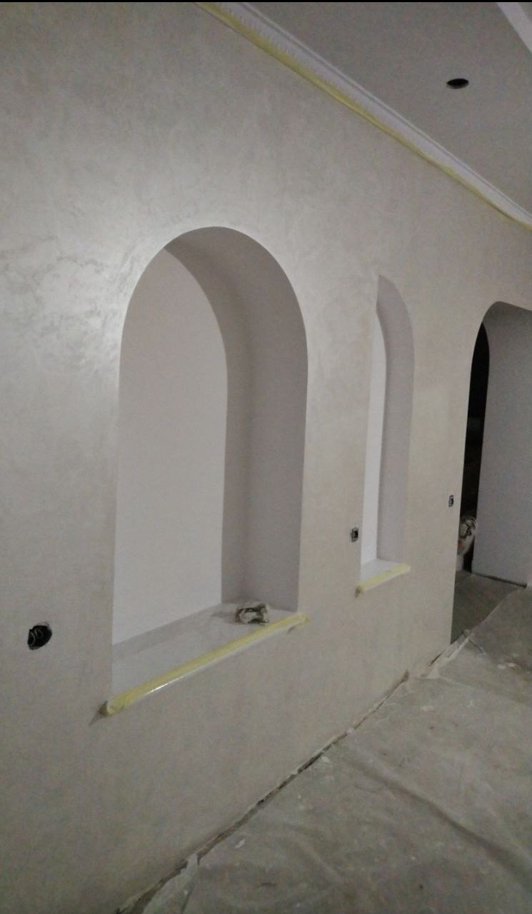 Ściana po gładzi z wnękami w kształcie łuków, zabezpieczona taśmą malarską, podłoga przykryta folią ochronną.