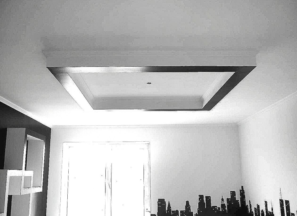 Sufit podwieszany w kształcie kwadratu z oświetleniem wnękowym, wykończony listwami przysufitowymi i czarną obwódką, na białej ścianie dekoracja w postaci czarnej panoramy miasta.
