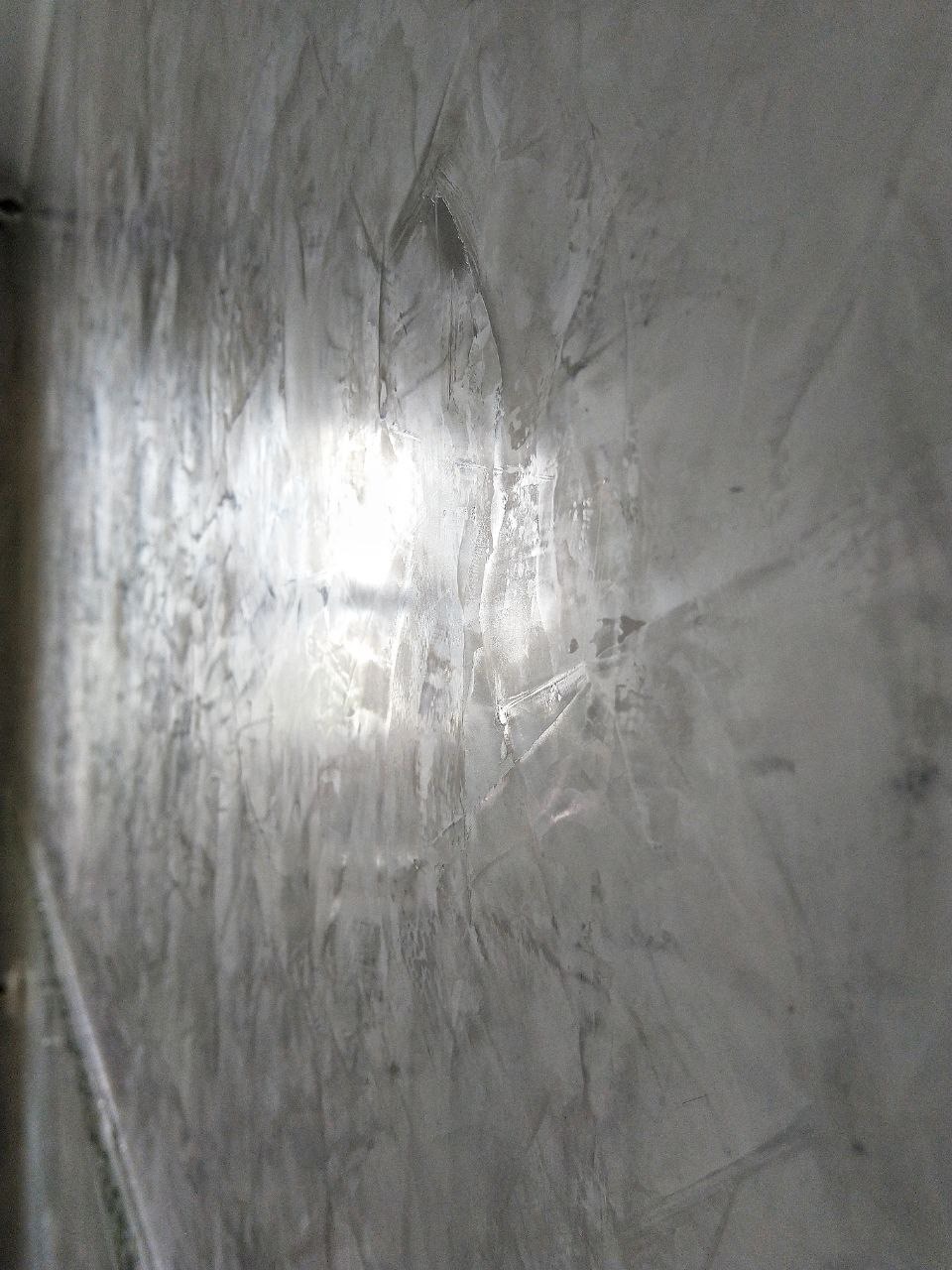 Ściana pokryta szarą, dekoracyjną strukturą z widocznymi smugami i odbiciem światła, ukazana pod kątem.