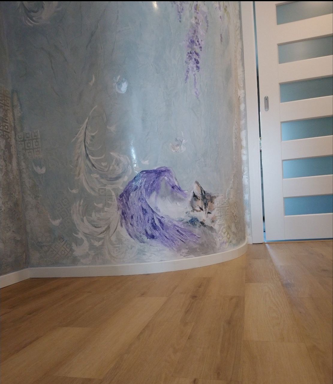 Dekoracyjna, strukturalna ściana z ręcznie malowanym motywem kota i wisterii, sąsiadująca z białymi drzwiami z przeszkleniami, na tle drewnianej podłogi.