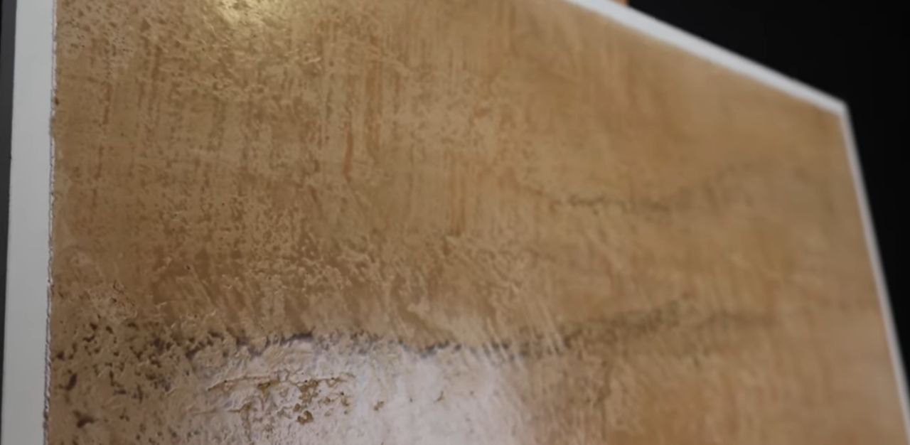 Beżowa ściana z dekoracyjną, nieregularną fakturą i poziomymi smugami, widoczna z bliska pod kątem.