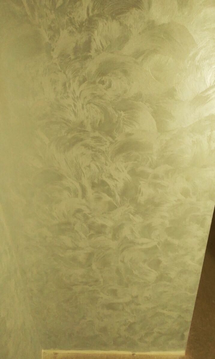 Ściana pokryta dekoracyjną, perłową farbą w odcieniach beżu, tworzącą efekt subtelnych, wirujących wzorów. Widoczny fragment podłogi z płytek w ciepłym odcieniu brązu.