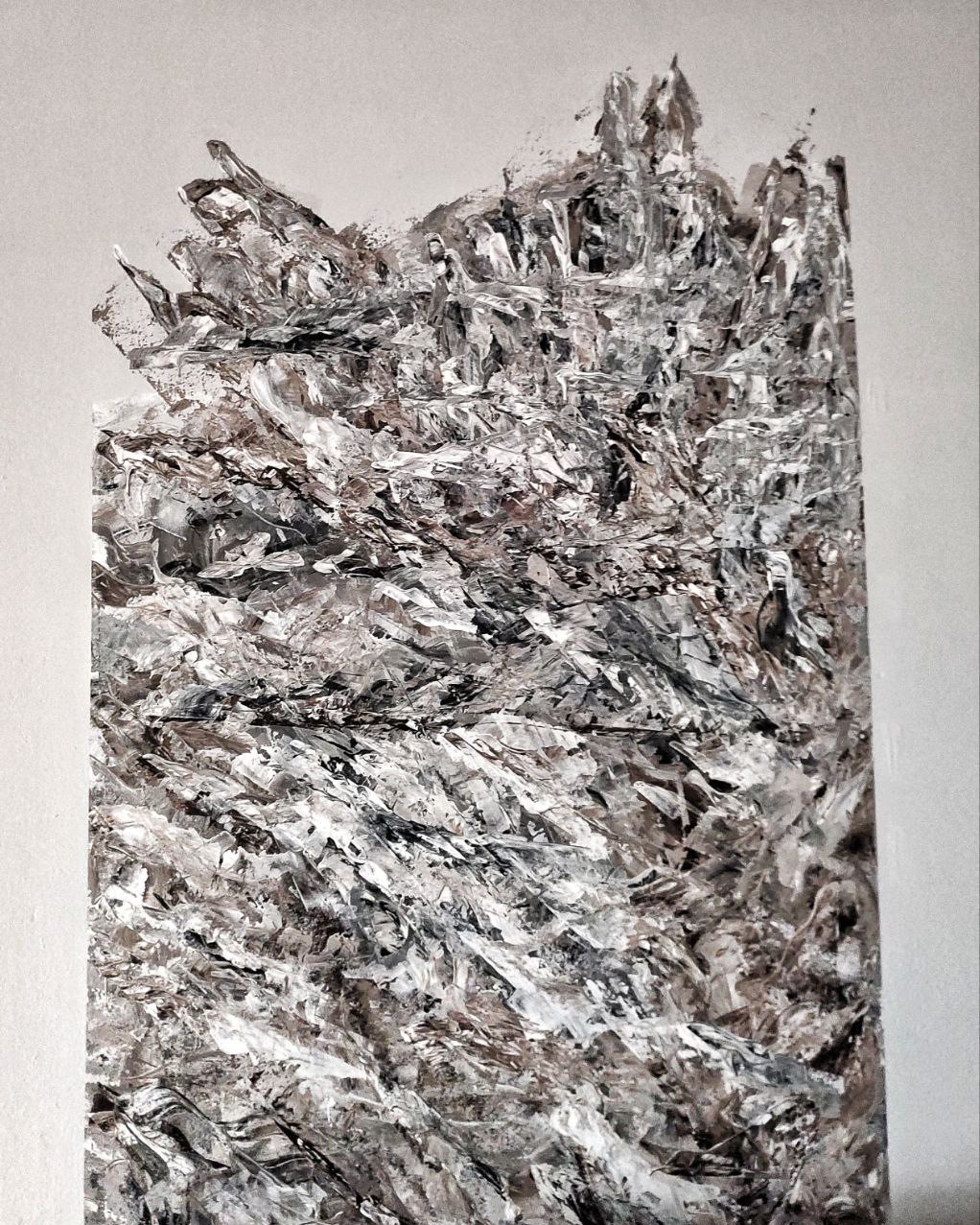 Nierównomiernie nałożona, gruba warstwa szaro-białej masy szpachlowej na ścianie, tworząca fakturę przypominającą górski krajobraz, z widocznymi śladami pędzla i nieregularnymi krawędziami.