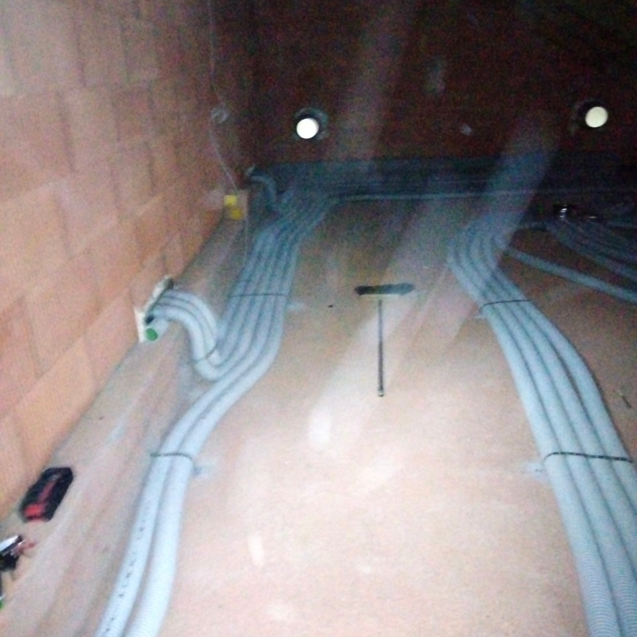 Rzędy szarych rur karbowanych ułożone na podłodze w surowym stanie, prawdopodobnie instalacja ogrzewania podłogowego lub inna instalacja podposadzkowa, widoczne narzędzia i elementy montażowe...