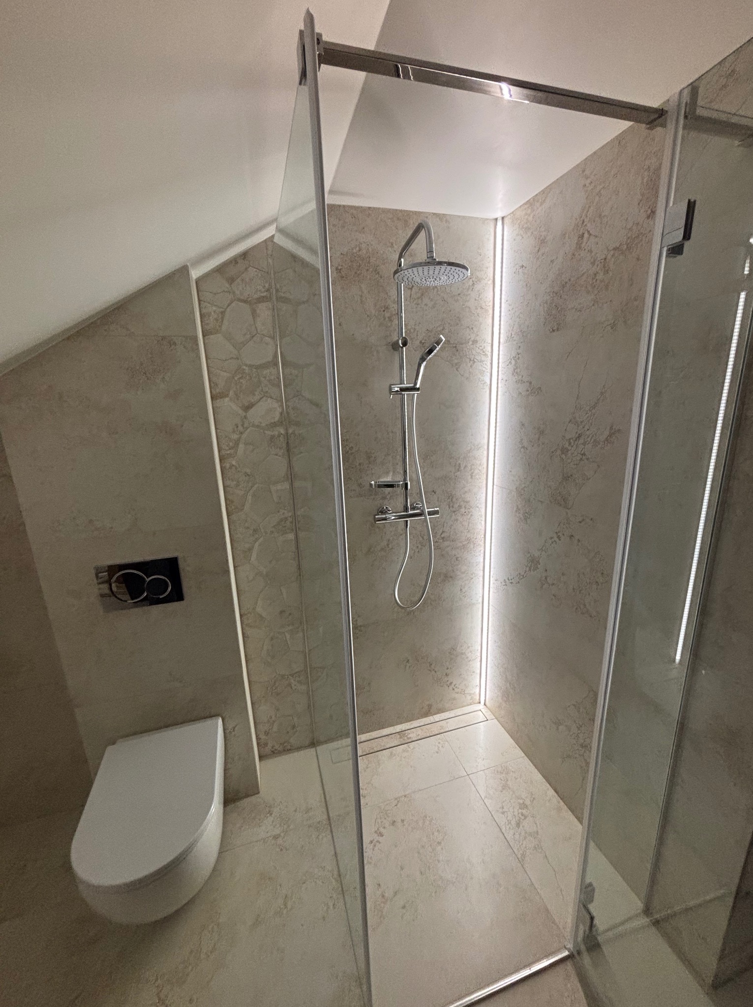 Nowoczesna kabina prysznicowa z deszczownicą i podświetleniem LED w wykończonej łazience na poddaszu. Uwagę zwraca wzór płytek imitujący kamień.