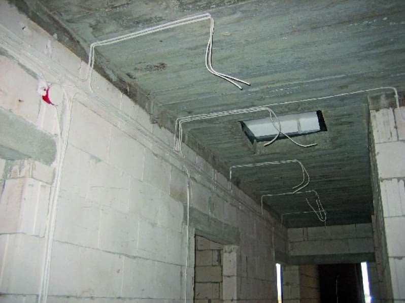 Surowy stan: białe kable elektryczne prowadzone po suficie i ścianach z betonu komórkowego w trakcie instalacji w budynku w stanie deweloperskim.