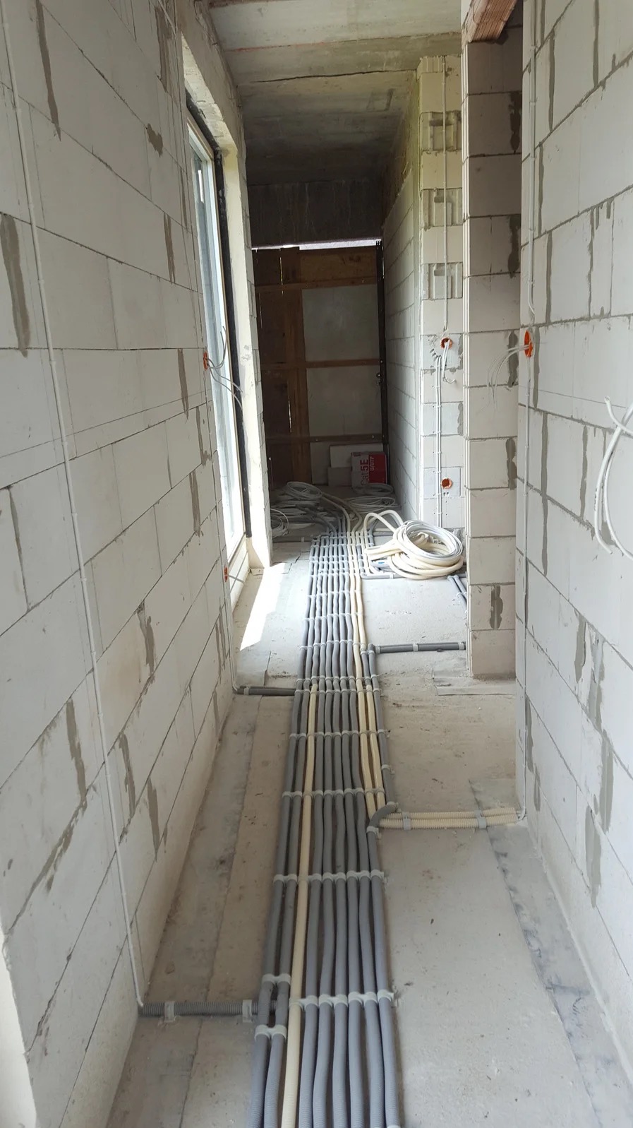 Korytarz w surowym stanie z widoczną instalacją elektryczną w peszlach ułożoną na podłodze i wyprowadzeniami na ścianach z betonu komórkowego.