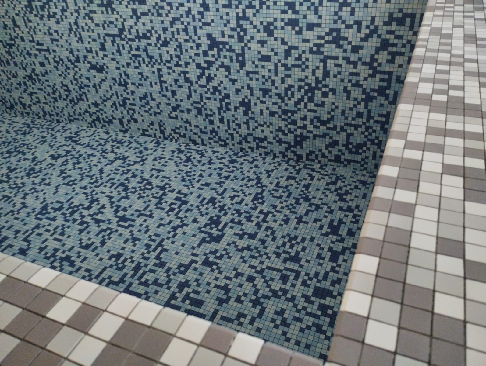 Wyłożona mozaiką w odcieniach błękitu i szarości niecka basenu, widok z góry na wykończone krawędzie.