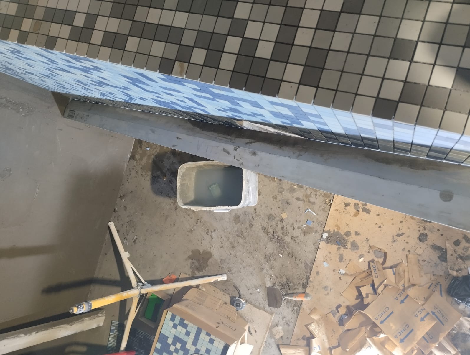 Układanie mozaiki w łazience w Nowej Soli, widok z góry na fragment ściany z ułożoną mozaiką, wiadro z wodą i narzędzia glazurnicze.