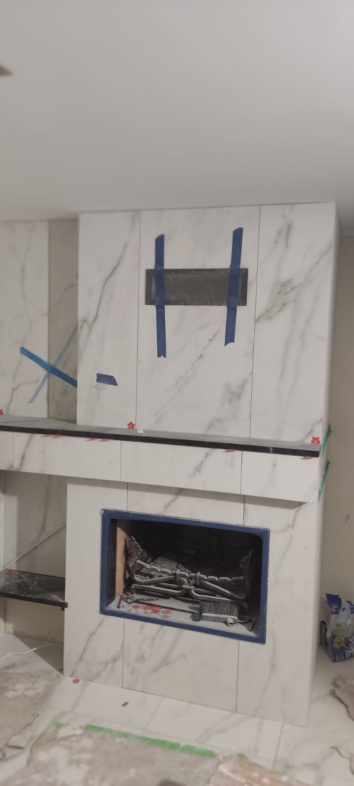 Wykończenie kominka płytkami imitującymi marmur, zabezpieczone taśmą malarską i poziomowane krzyżykami glazurniczymi.