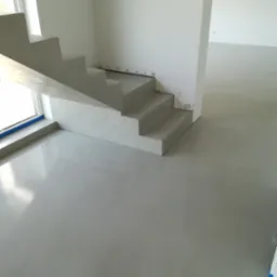 Minimalistyczne, szare schody w nowoczesnym wnętrzu. Widoczne gładkie, jednolite powierzchnie ścian i podłogi. W tle surowy stan wykończenia.