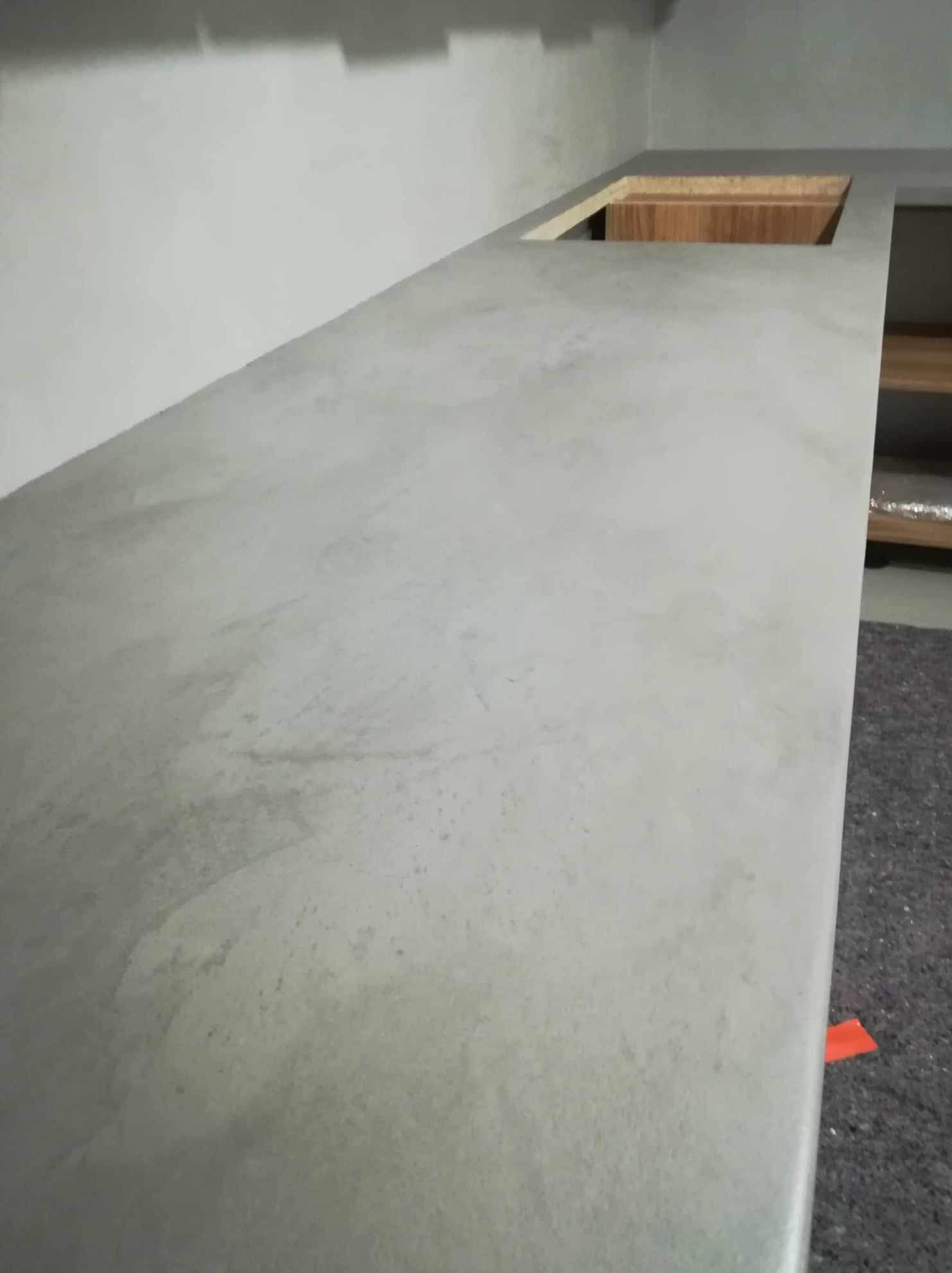 Blat kuchenny z szarego betonu architektonicznego z wycięciem na zlew, widoczny fragment szafki i szara ściana w tle. Minimalistyczny design.