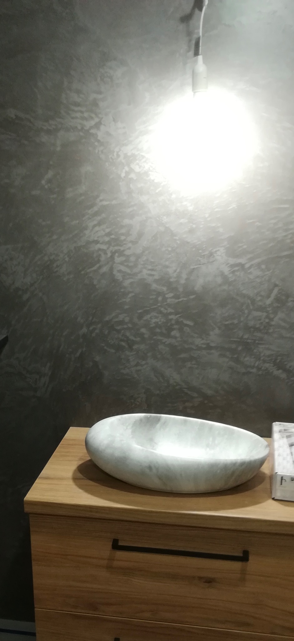 Wykończona łazienka: dekoracyjna szara ściana z efektem stiuku weneckiego, marmurowa umywalka nablatowa na drewnianej szafce z czarnymi uchwytami.