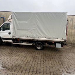 Paweł Jóźwiak - Biały samochód dostawczy z plandeką na mokrym brukowanym podwórku, widoczne ślady użytkowania i zabrudzenia.