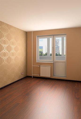 Pusty pokój po remoncie: brązowe panele podłogowe, beżowe ściany z delikatnym wzorem, białe okno balkonowe z widokiem na miasto.