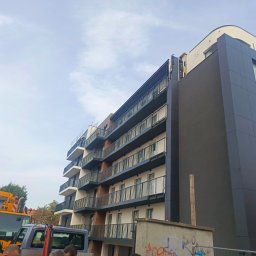 GRUPA POMORSKA PERłA SP. Z O.O. - Wielopiętrowy budynek mieszkalny z balkonami i elewacją w trakcie prac wykończeniowych, widoczny dźwig budowlany i fragment ogrodzenia.