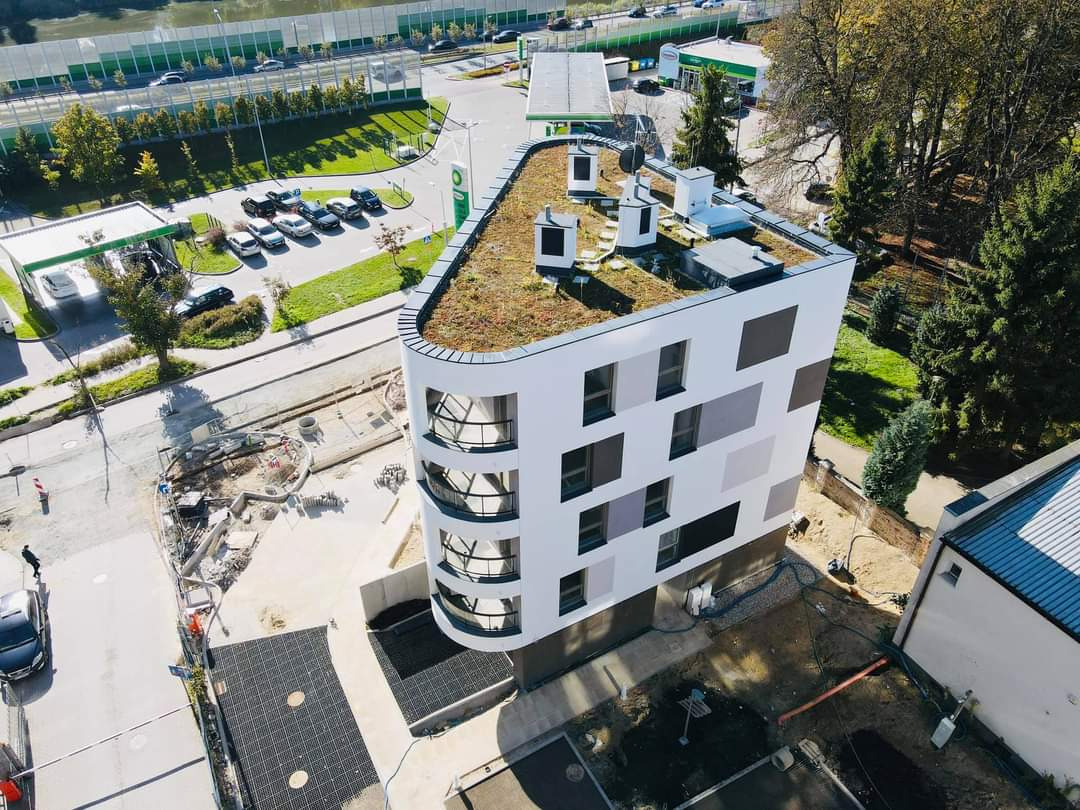 Widok z góry na nowoczesny budynek z zielonym dachem w pobliżu stacji benzynowej BP, z placem budowy w tle.
