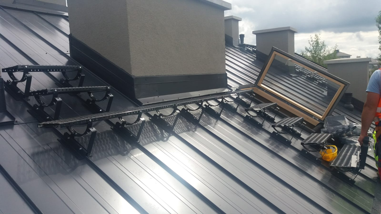 Montaż okna dachowego na metalowym dachu z zainstalowanymi stopniami kominiarskimi i ławą kominiarską