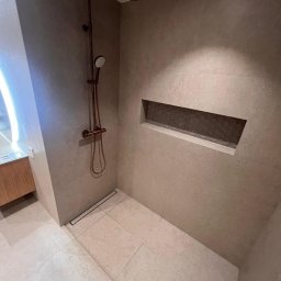 Artur Hinc - Nowoczesna kabina prysznicowa z deszczownicą w kolorze miedzi, beżowe płytki wielkoformatowe, odpływ liniowy i wnęka w ścianie wykończona heksagonalnymi płytkami.