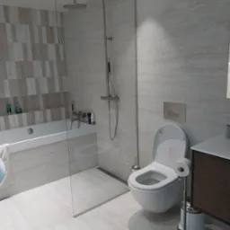 Jasna łazienka w Wielkim Gowinie z kabiną prysznicową typu walk-in, wiszącą toaletą i umywalką z szafką w odcieniach brązu, wykończona płytkami imitującymi marmur.