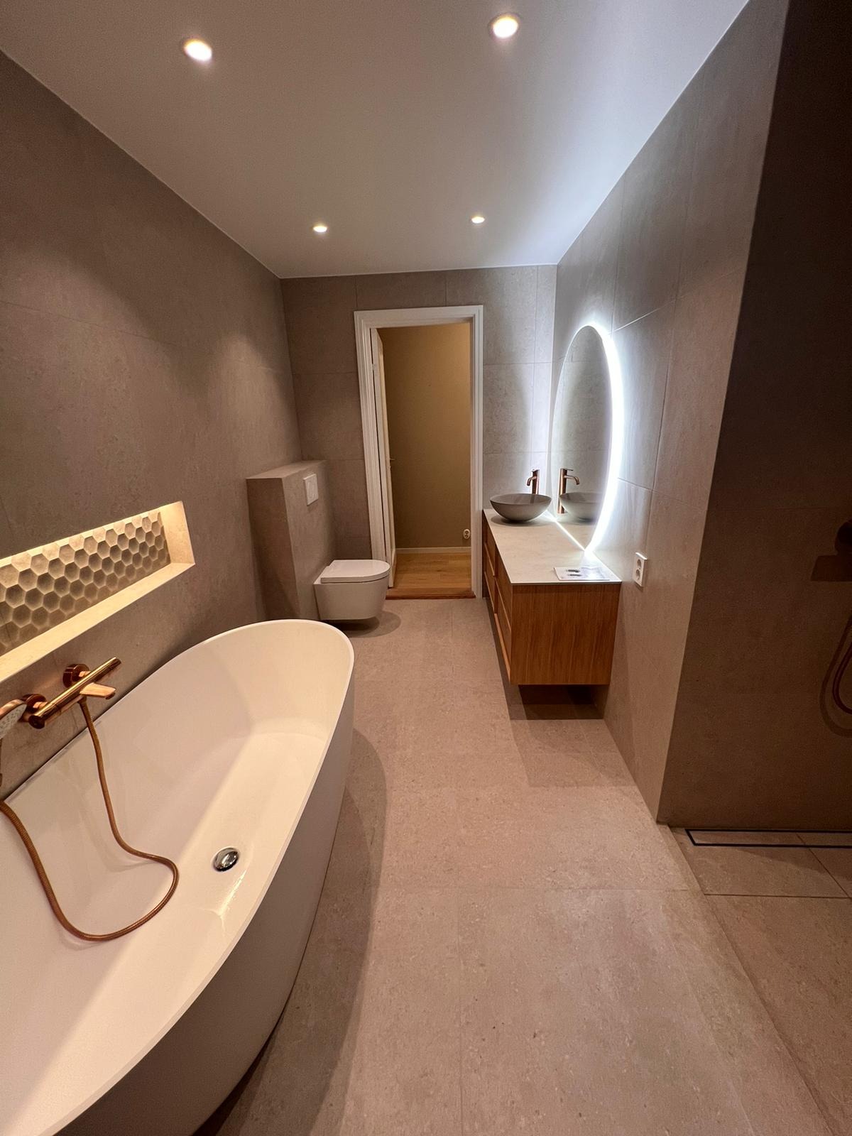 Nowoczesna łazienka z wolnostojącą wanną, umywalką nablatową z podświetlanym lustrem i heksagonalnymi płytkami w niszy ściennej.