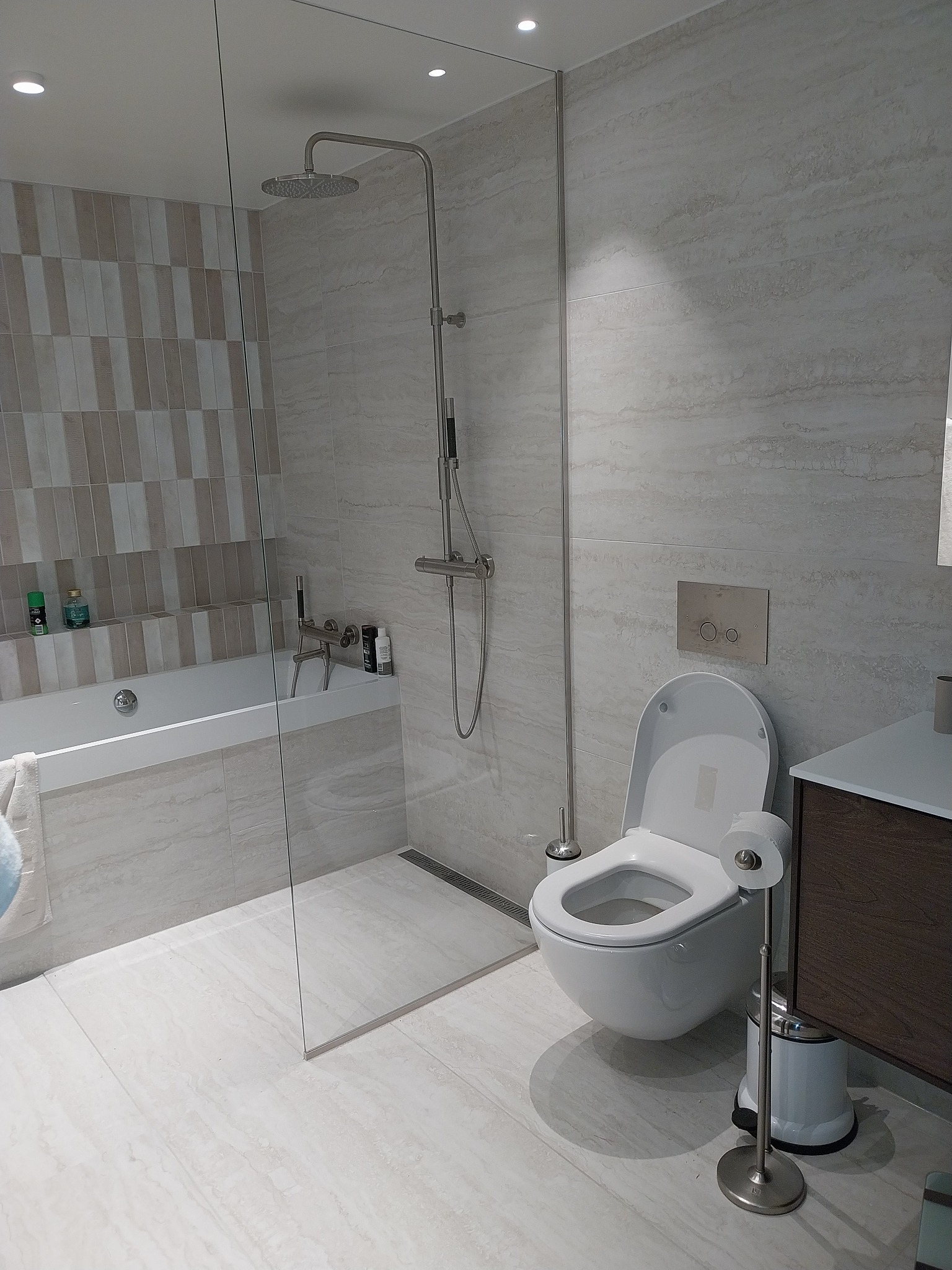 Jasna łazienka w Wielkim Gowinie z kabiną prysznicową typu walk-in, wiszącą toaletą i umywalką z szafką w odcieniach brązu, wykończona płytkami imitującymi marmur.