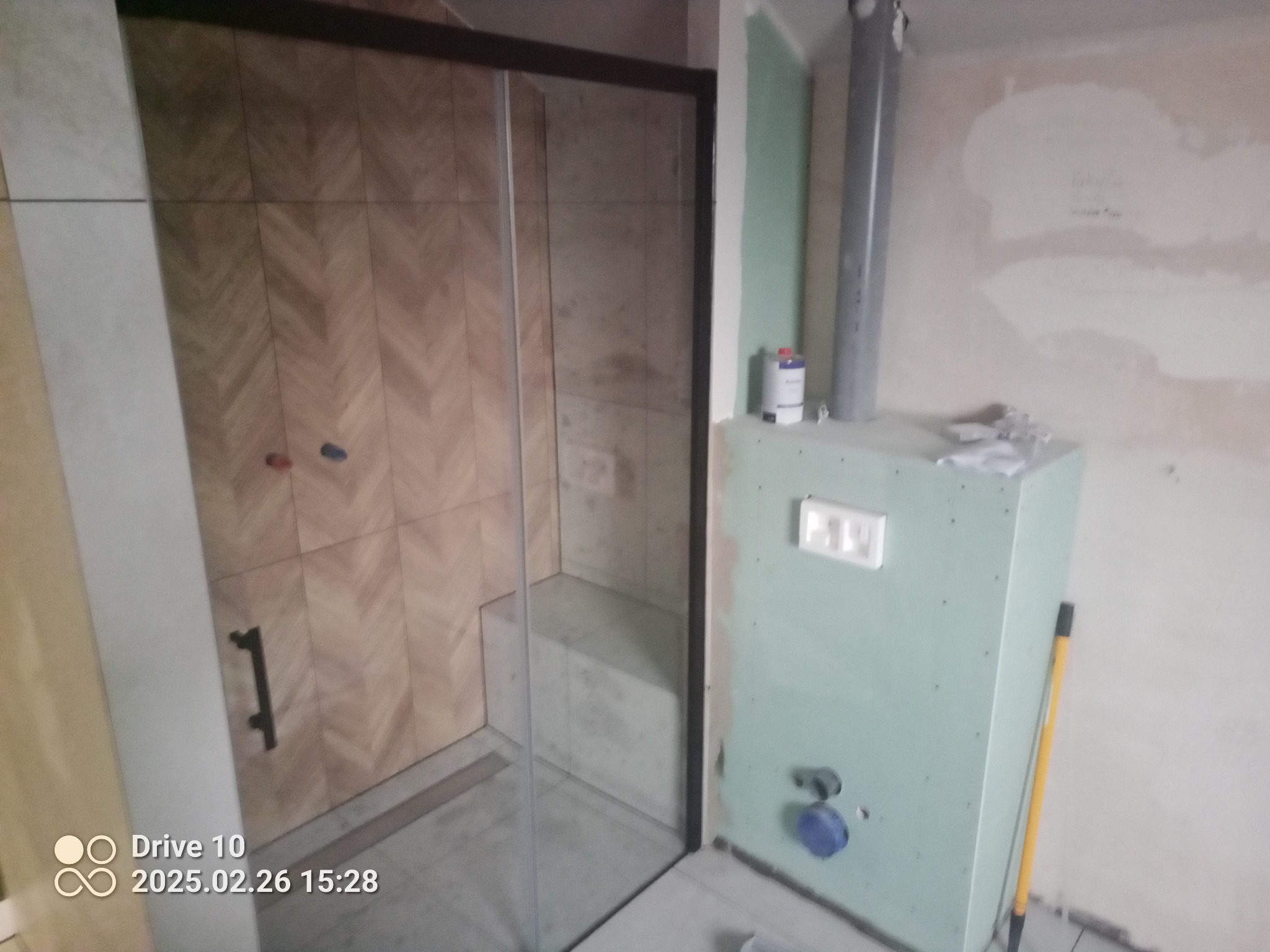 Montaż kabiny prysznicowej z wzorzystymi płytkami w trakcie wykańczania łazienki, widoczne niedokończone ściany z płyt gipsowo-kartonowych i instalacje hydrauliczne.