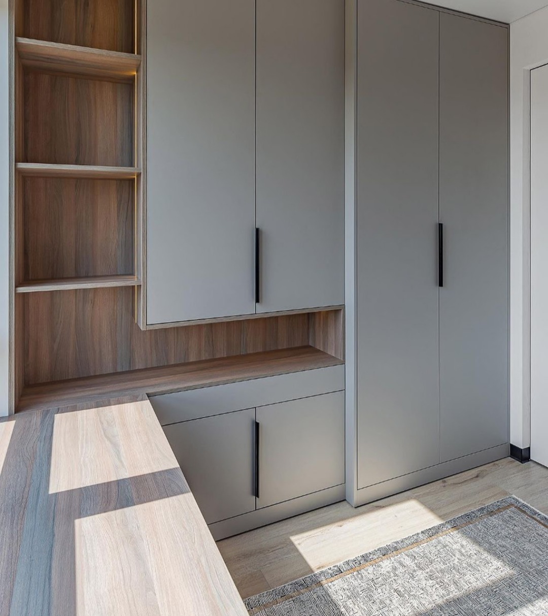 Szara zabudowa meblowa z szafkami, półkami z podświetleniem LED i blatem roboczym w minimalistycznym stylu, widoczny fragment dywanu.