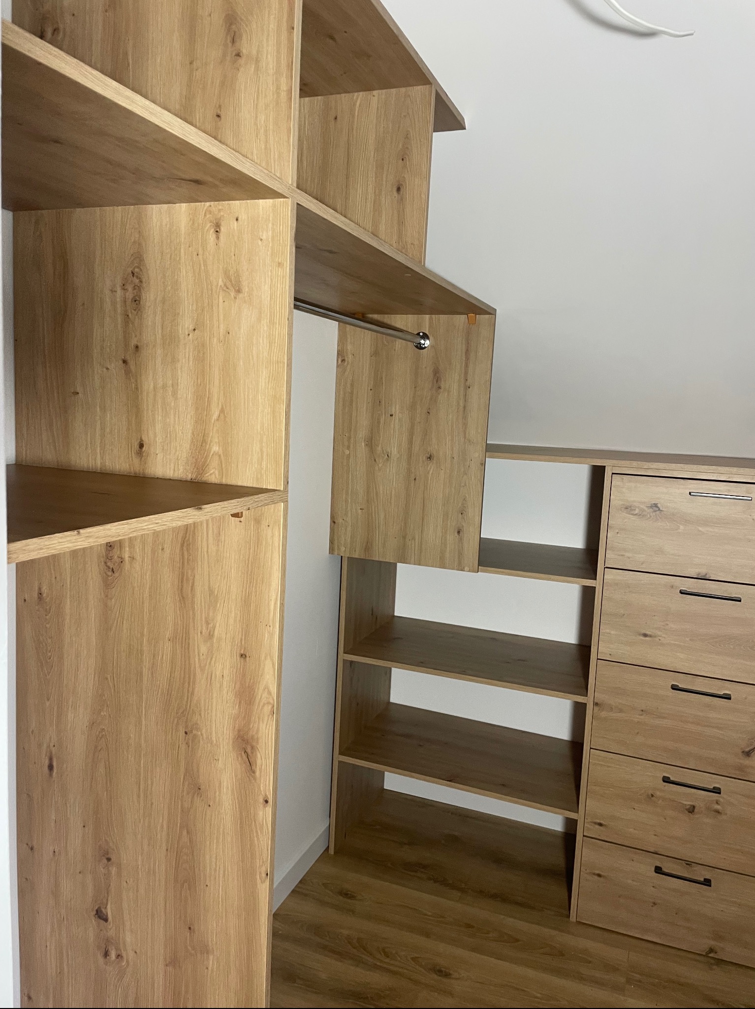 Jasna, drewniana szafa wnękowa z półkami i szufladami, widok z bliska na wnętrze garderoby. Minimalistyczne uchwyty, naturalne wykończenie drewna.