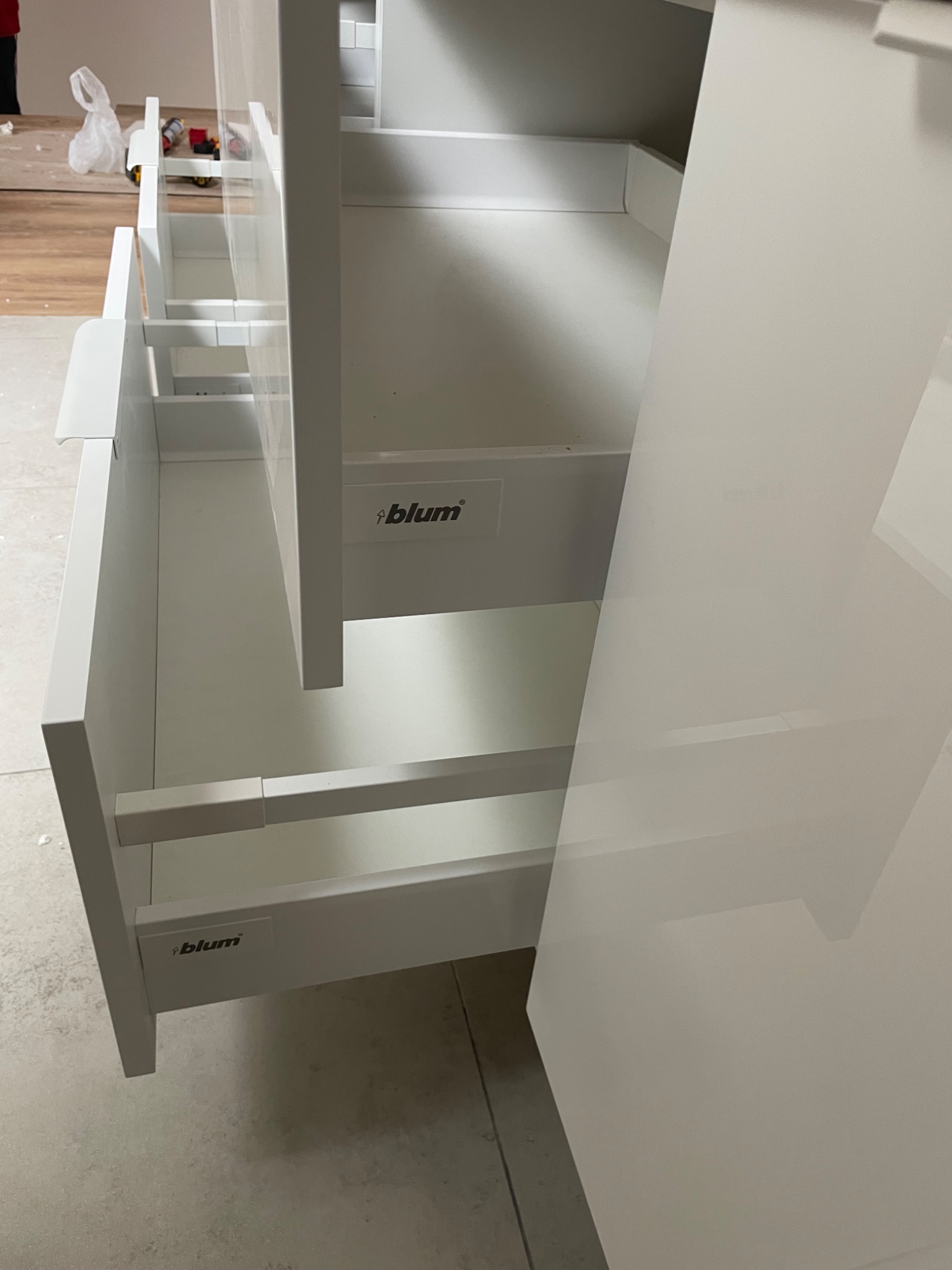 Białe, otwarte szuflady z systemem Blum w szafce. Widoczne detale montażu i wykończenia. Ujęcie z bliska, podkreślające jakość wykonania i funkcjonalność.