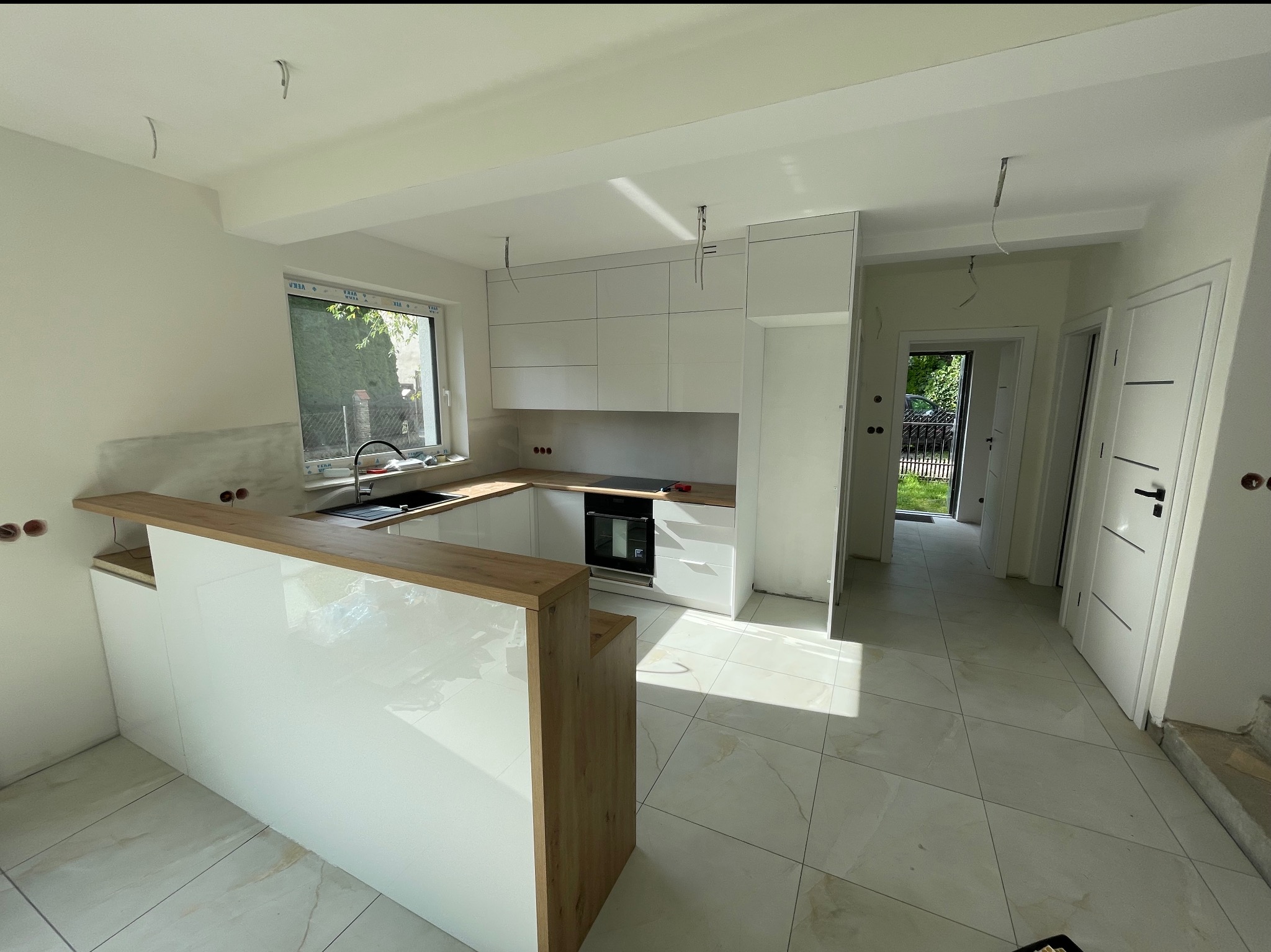 Nowoczesna kuchnia z białymi szafkami i drewnianym blatem w Jaszczurowej. Widoczne niedokończone wykończenia, co dodaje autentyczności zdjęciu.