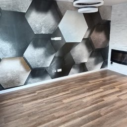 Master-Bud - Nowoczesne wnętrze: parkiet w odcieniach brązu, ściana z heksagonalnym wzorem 3D w szarościach, designerska lampa sufitowa i imitacja kominka.