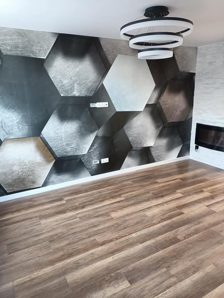 Nowoczesne wnętrze: parkiet w odcieniach brązu, ściana z heksagonalnym wzorem 3D w szarościach, designerska lampa sufitowa i imitacja kominka.