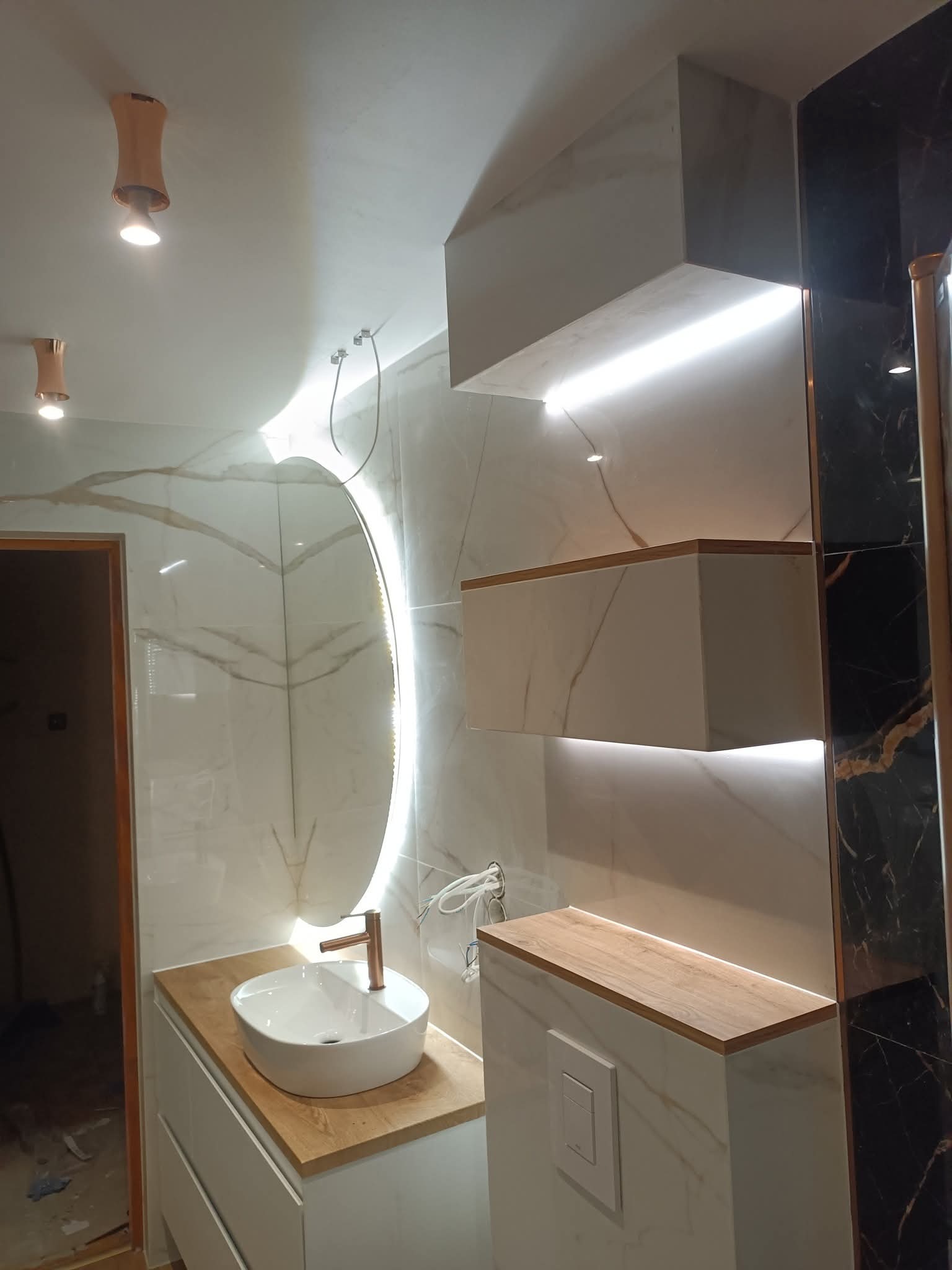 Nowoczesna łazienka po remoncie w Solcu-Zdroju. Białe szafki z drewnianym blatem, okrągłe lustro z podświetleniem LED i marmurowe płytki.