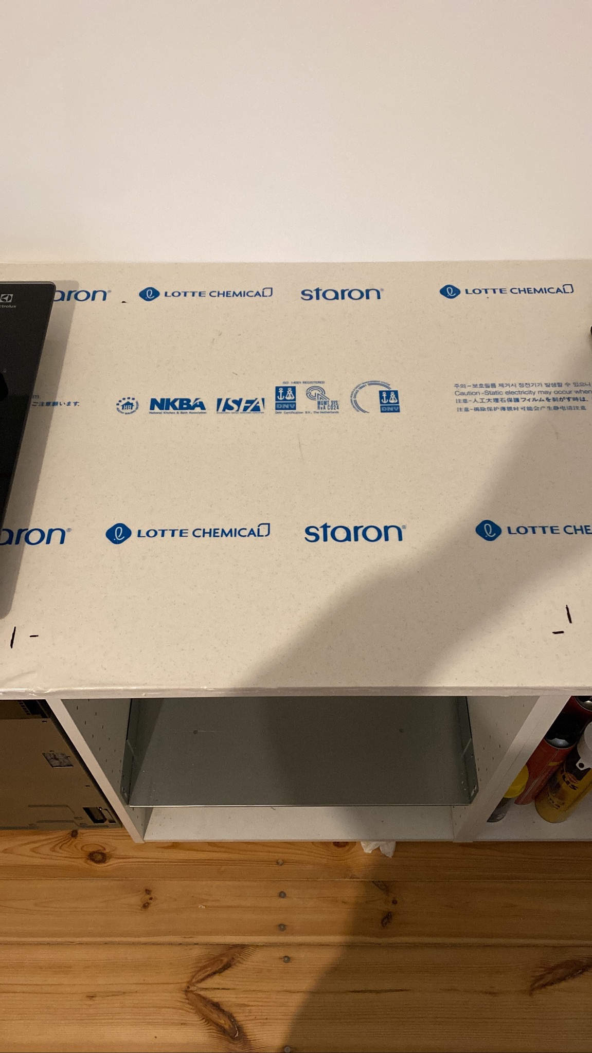 Montaż blatu kuchennego Staron Lotte Chemical z certyfikatami NKBA i DNV, widoczne szafki i drewniana podłoga. Blat z folią ochronną.