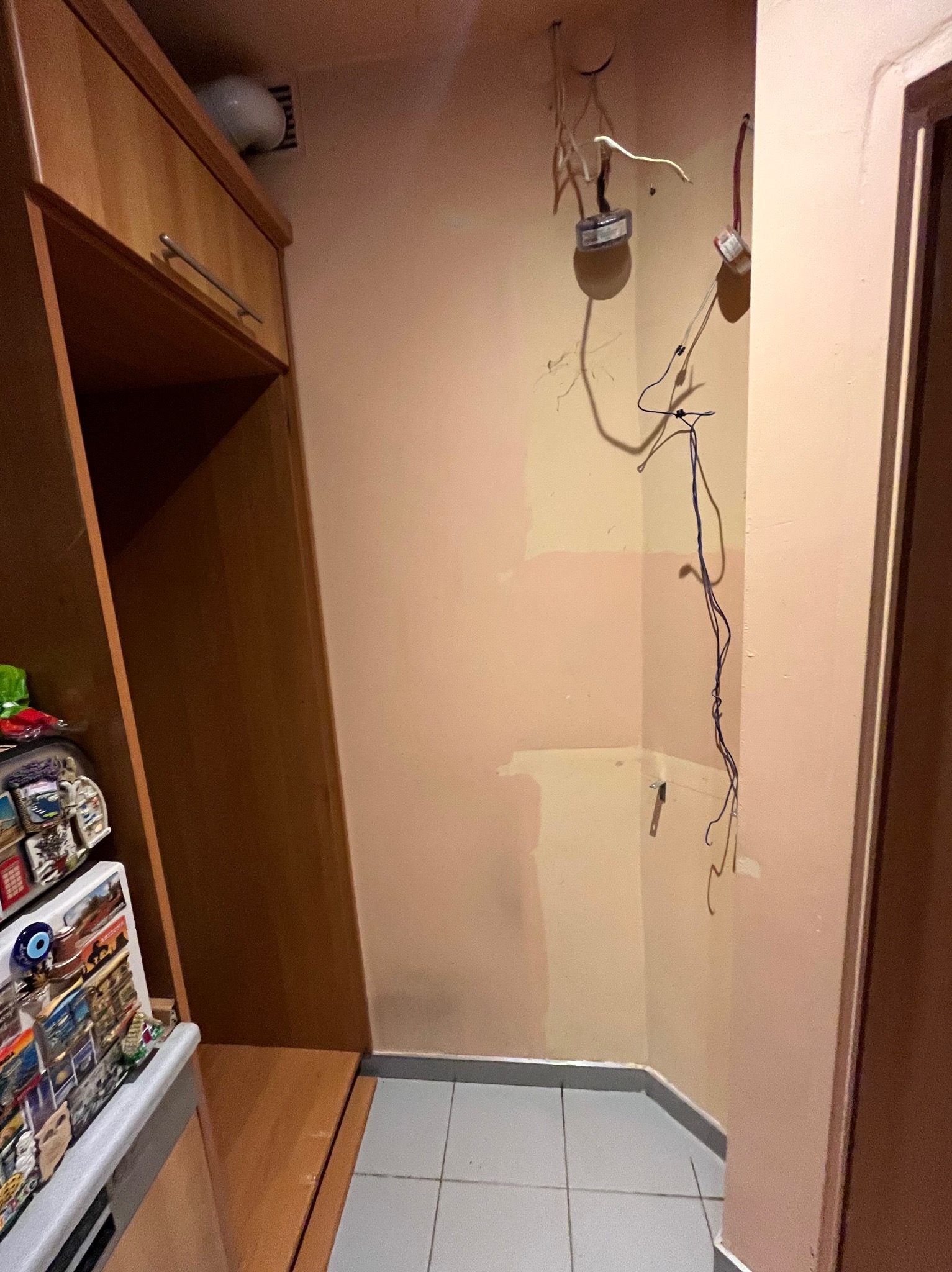 Niedokończone prace w rogu pokoju z odsłoniętymi przewodami elektrycznymi, fragmentem szafki z magnesami i przygotowanymi ścianami do dalszych prac.
