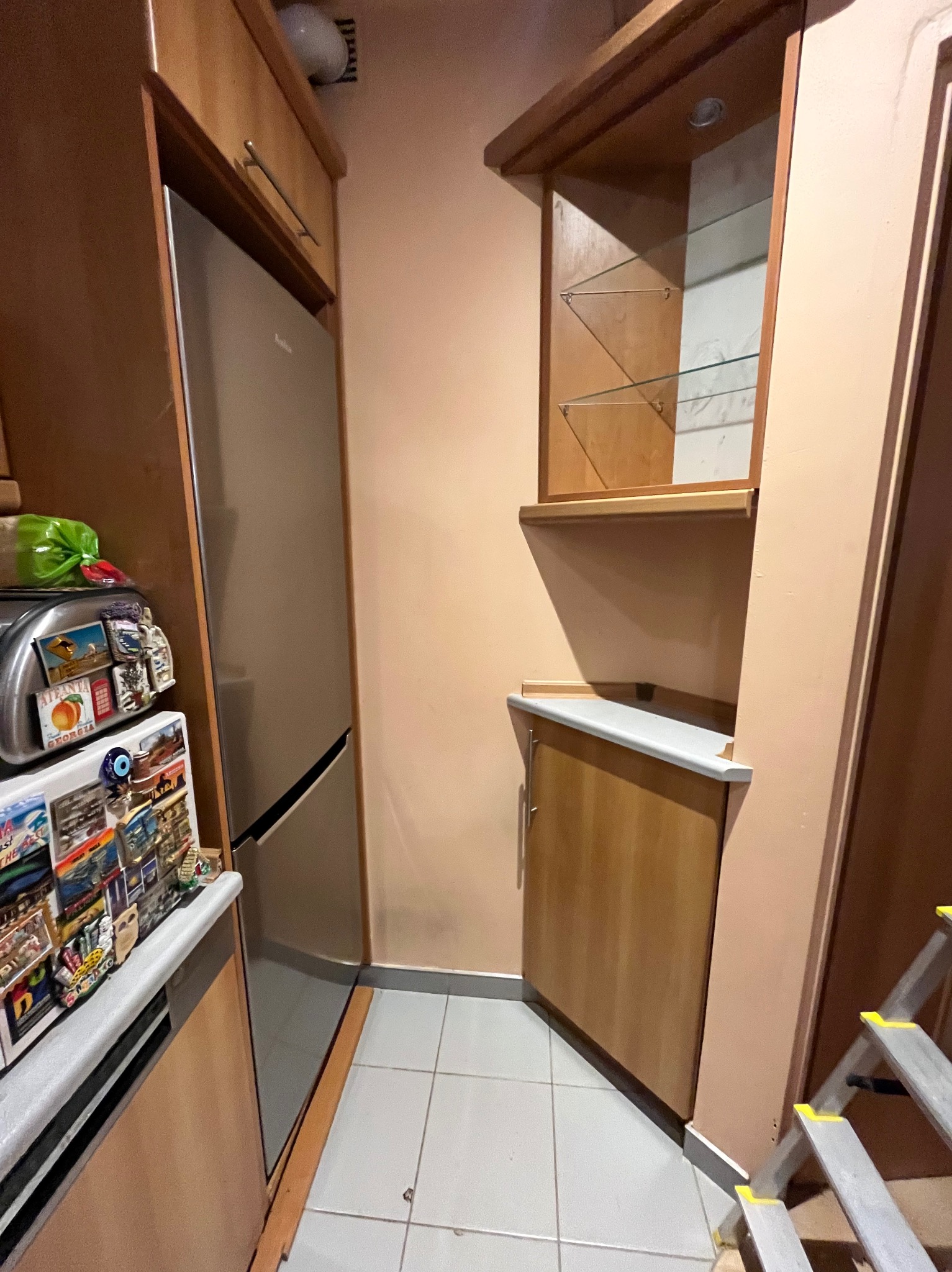 Wnętrze kuchni z drewnianymi szafkami, lodówką obłożoną magnesami i fragmentem drabiny malarskiej