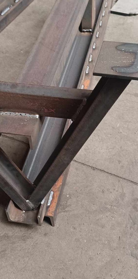 Fragment konstrukcji stalowej z widocznymi spawami, spawana rama z profili zamkniętych i ceowników, surowy beton na podłożu.