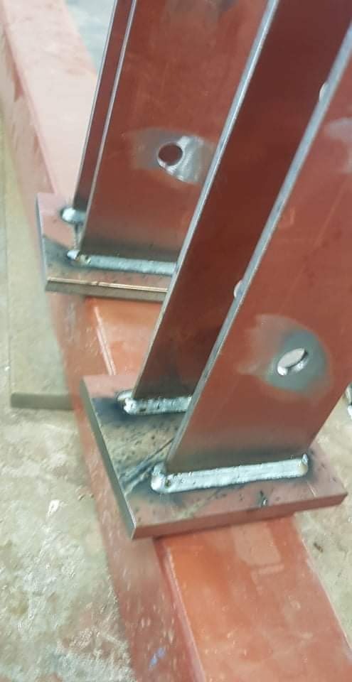 Czerwona, stalowa konstrukcja spawana z widocznymi otworami, ukazująca połączenia elementów pod kątem.