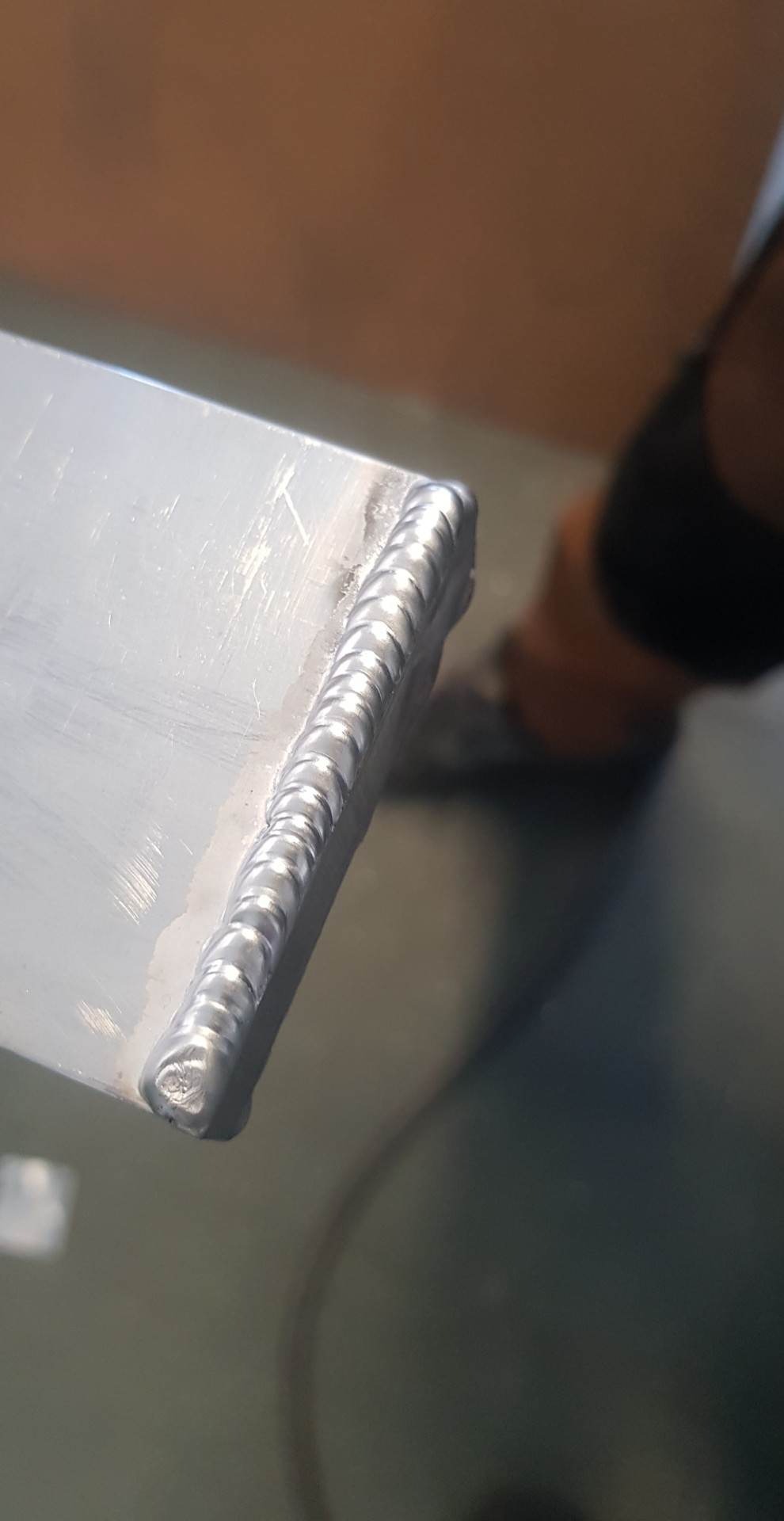 Połączenie spawane na krawędzi metalowego elementu z widocznymi śladami obróbki, ukazujące regularne, półokrągłe spoiny.