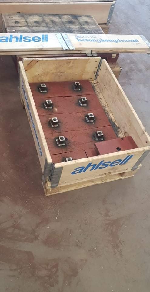 Drewniana skrzynia z elementami metalowymi, prawdopodobnie do konstrukcji betonowych, z widocznym logo firmy Ahlisell.